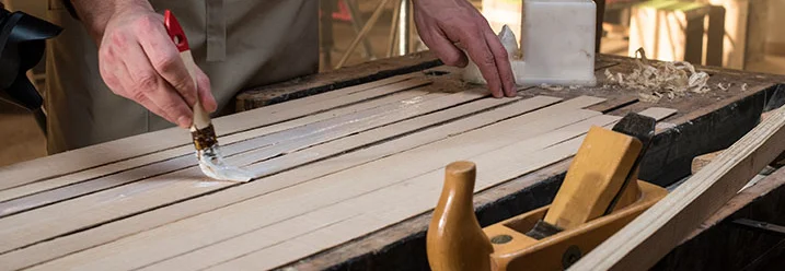 Person trägt Leim auf Holzlatten auf